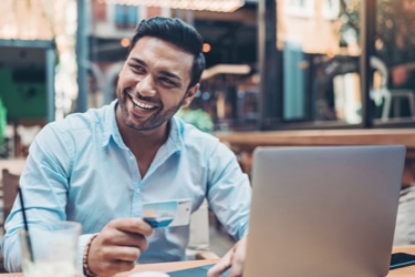 A person sitting with one hand on a laptop and their other hand holding a credit card